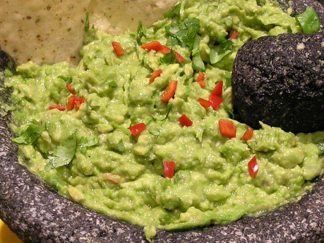 A close up of guacamole in a mortar and pestle with tortilla chips.