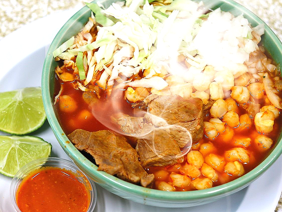 A bowl of soup with meat , beans , cabbage and cheese on a plate.