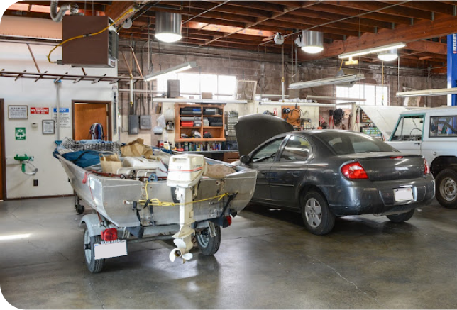 A boat is on a trailer in a garage next to a car | Bill's Auto Electric Repair Inc