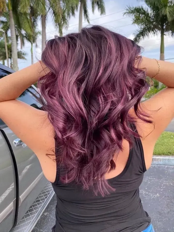 A woman with purple hair is standing in front of a car.