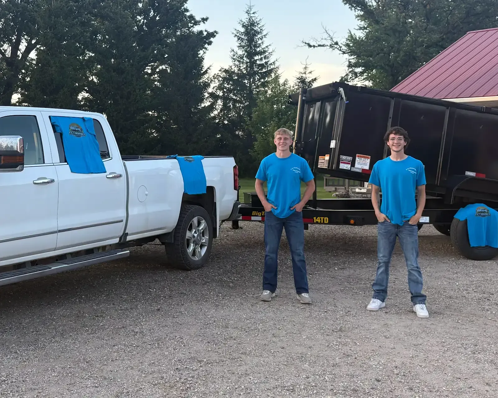 Two men in blue shirts are standing in front of a truck and trailer.