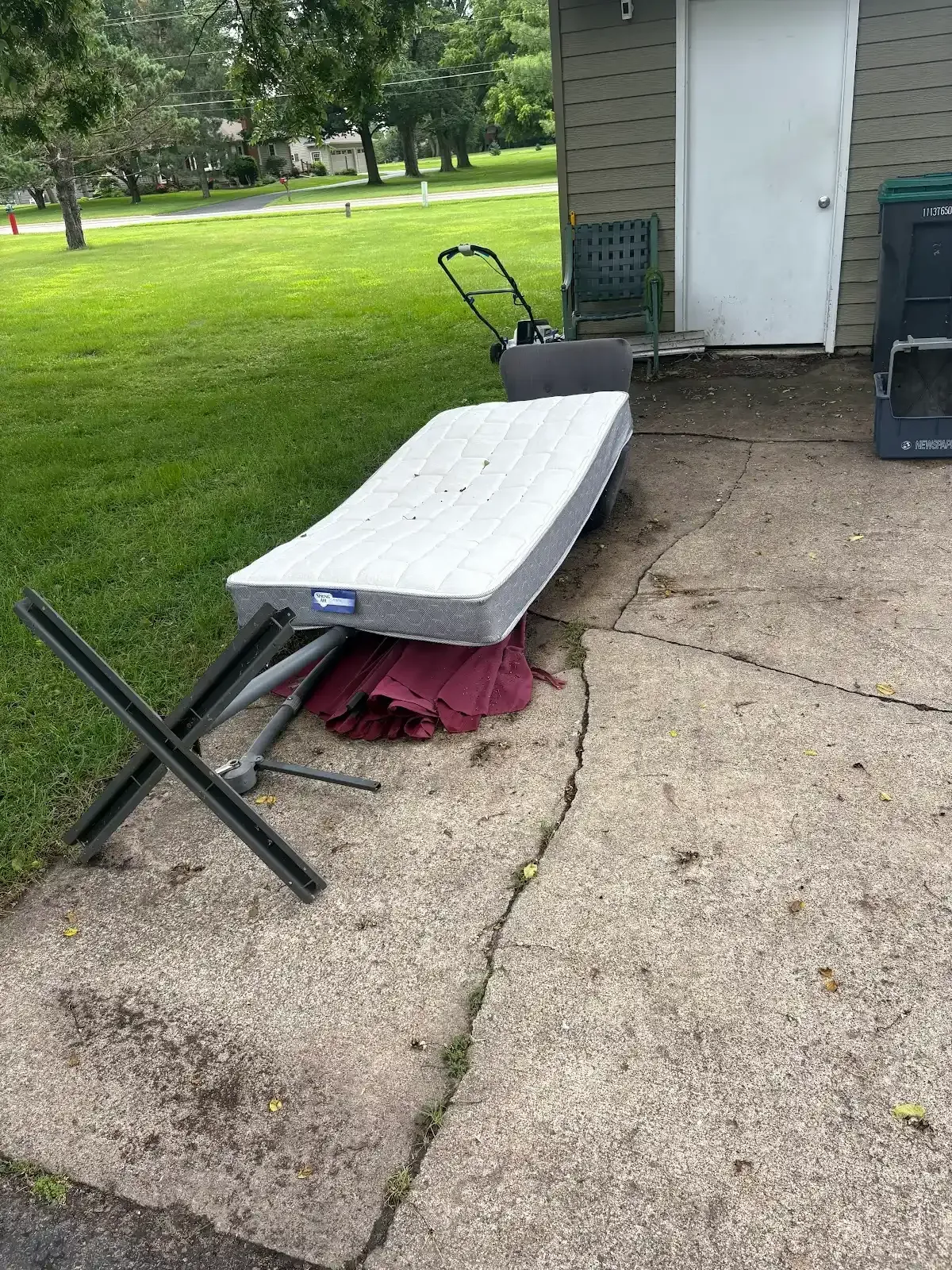 A mattress is sitting on the sidewalk next to a chair.