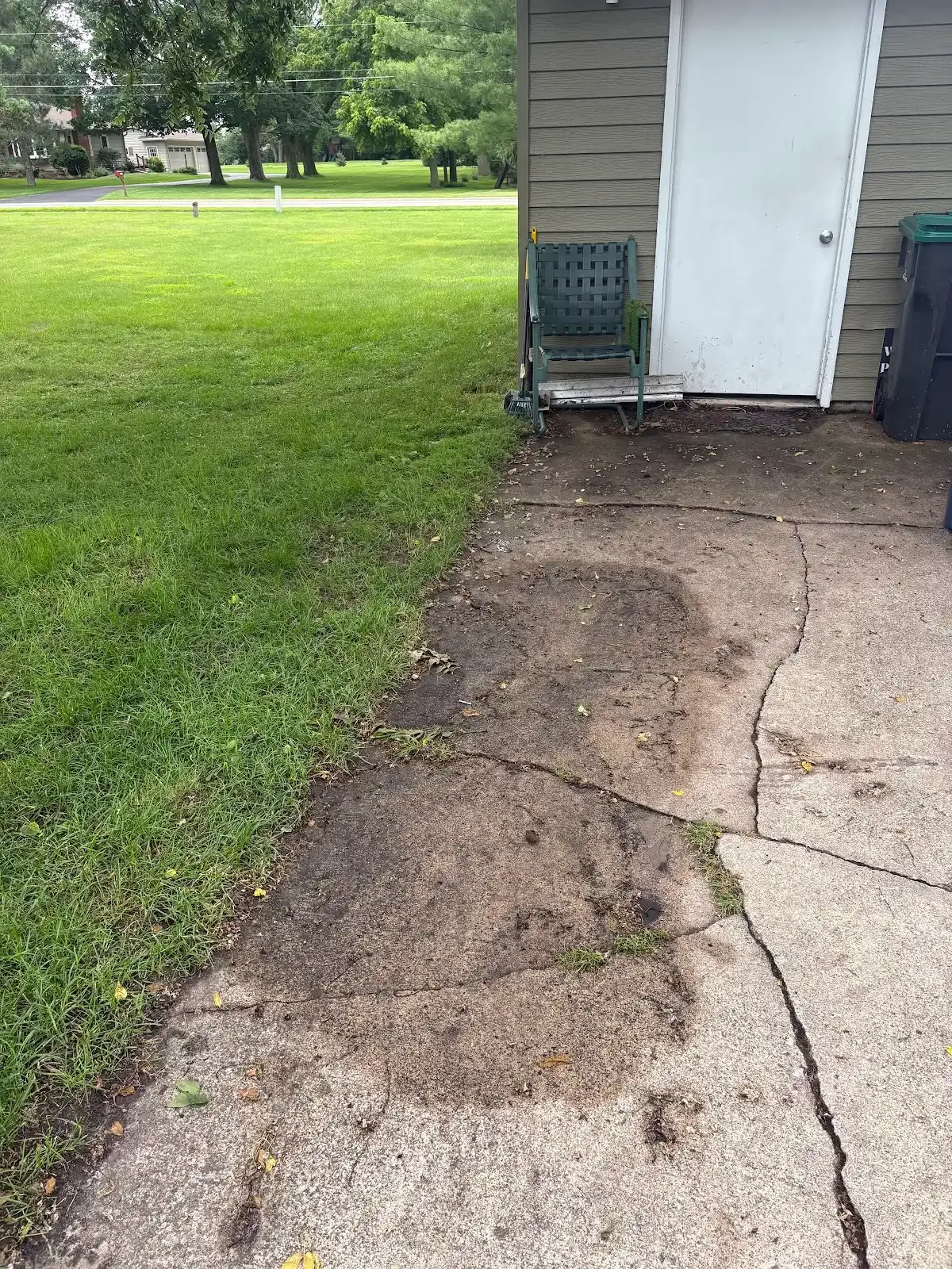 A concrete walkway leading to a shed with a chair in front of it.