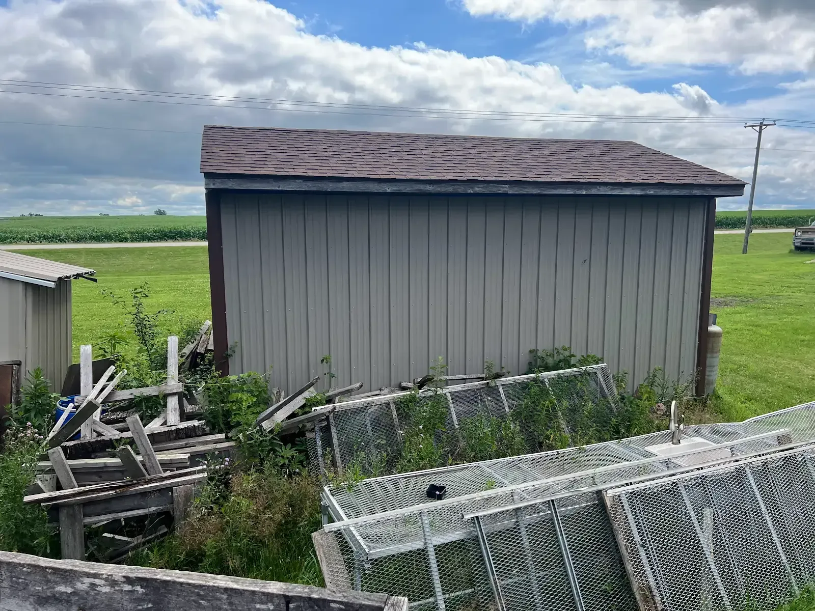 A shed is sitting in the middle of a field next to a chain link fence.