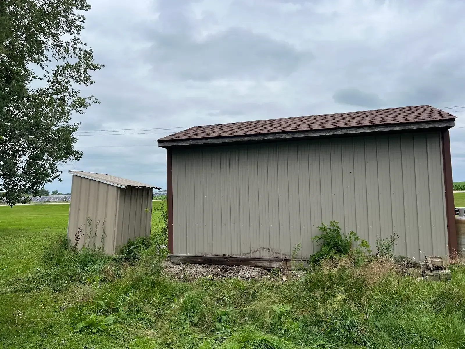 Two sheds are sitting in the middle of a grassy field.