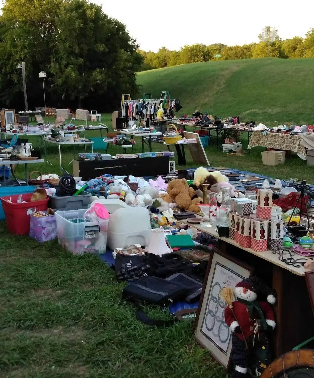 Yard sale with various items on display in a grassy field.
