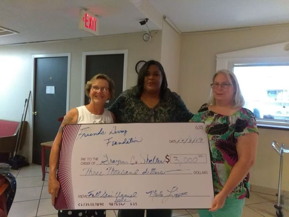 Three women holding a large check from the Friends Raves Foundation for $3,000, indoors.