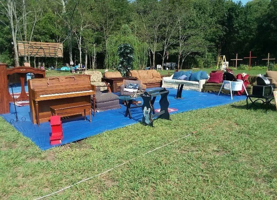 Outdoor yard sale with furniture displayed on a blue tarp in a grassy area with trees in the background.
