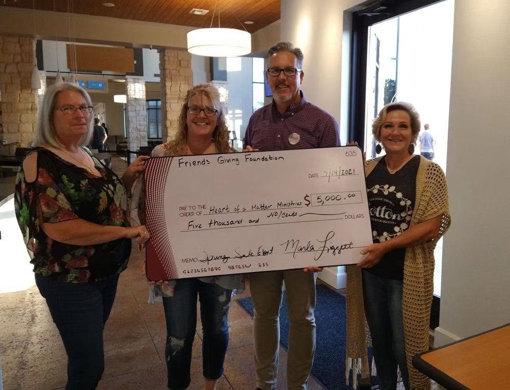 Four people holding a large check for the Friends Caring Foundation in a bright lobby.