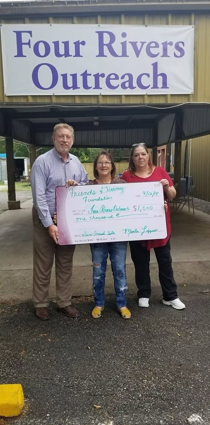 Three people holding a large check under a banner that reads,