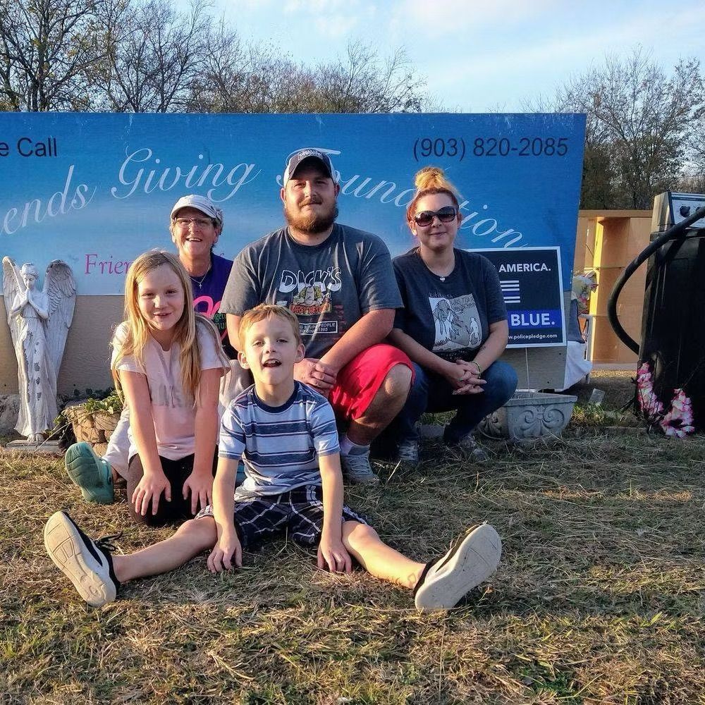 Group of five smiling people in front of a blue Friends Giving Foundation sign.
