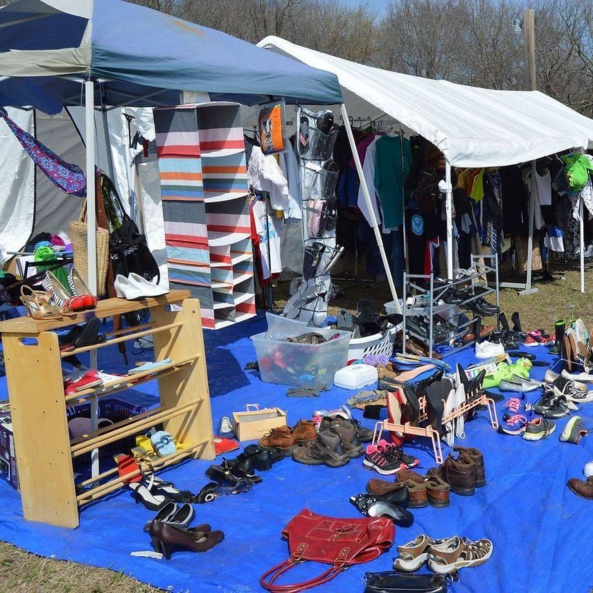 Outdoor yard sale with clothing, shoes, and various items displayed on tables and tarps under white canopies.