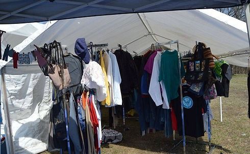 Clothing displayed on racks under a white tent; outdoor market setting.