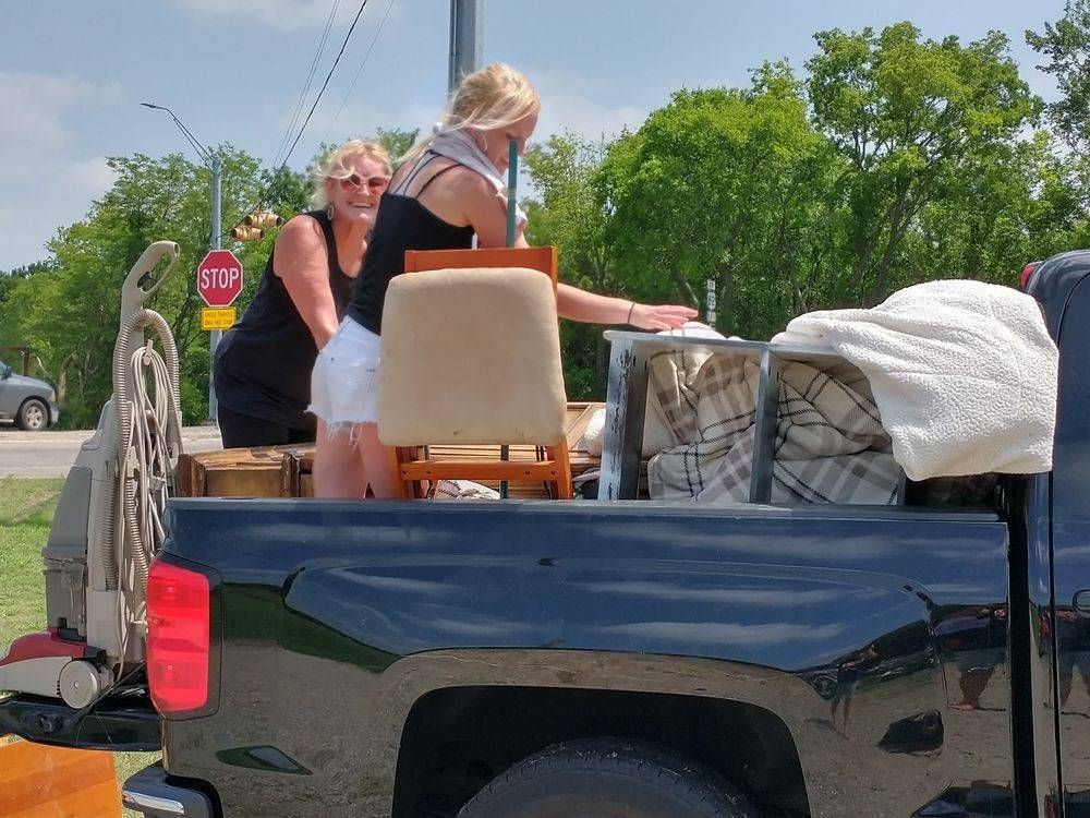 Two people loading furniture into a black pickup truck outdoors near a road with a stop sign.