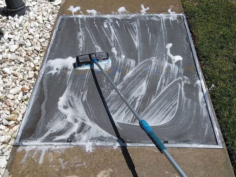 A brush is being used to clean a screen door