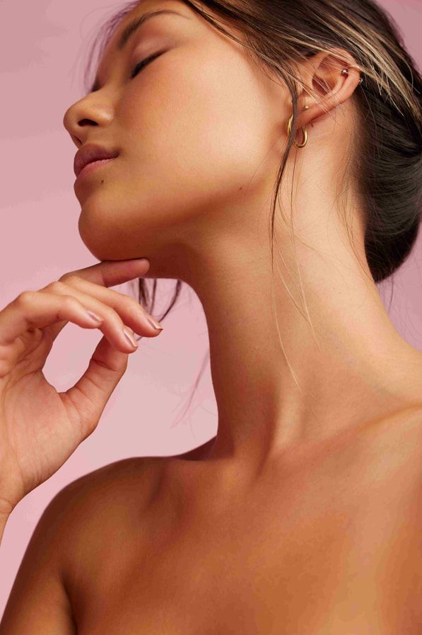 A Woman is Touching Her Neck With Her Hand and Wearing Earrings — Aria Skin & Beauty in Gympie, QLD