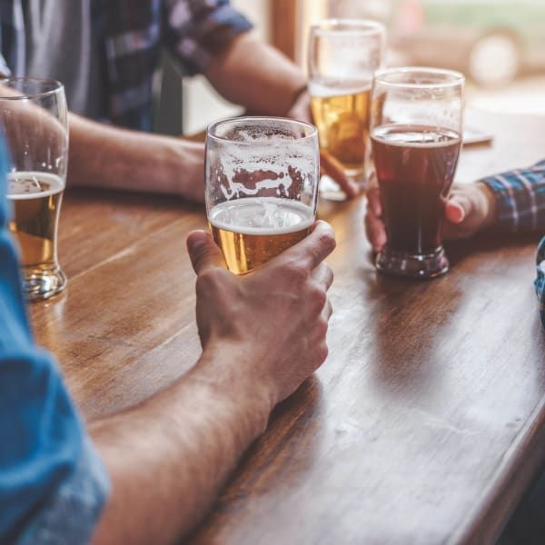 Several people holding glasses of beer during a social gathering at a wooden table.