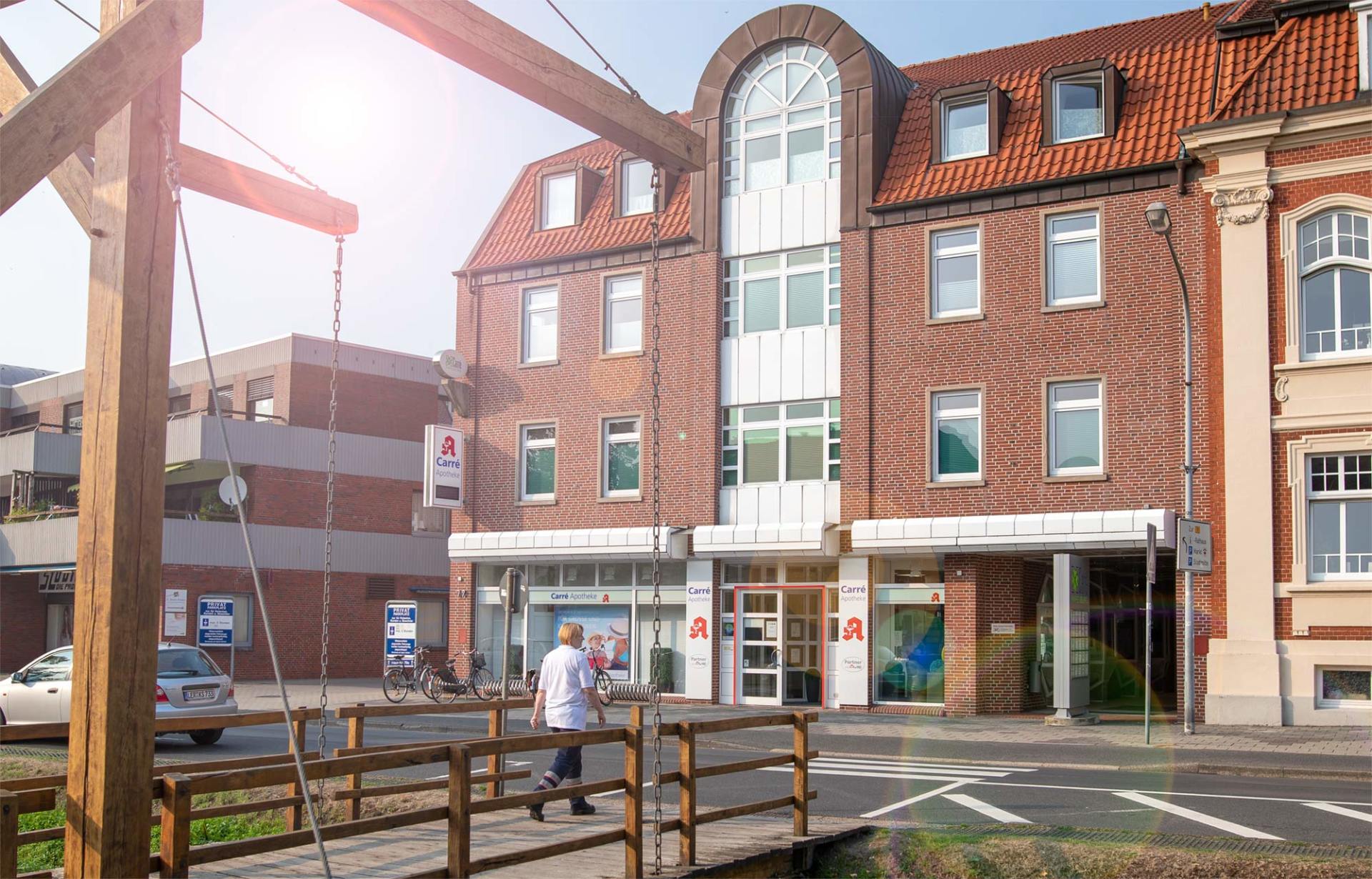 Ein Mann geht über eine Holzbrücke vor einem großen Backsteingebäude.