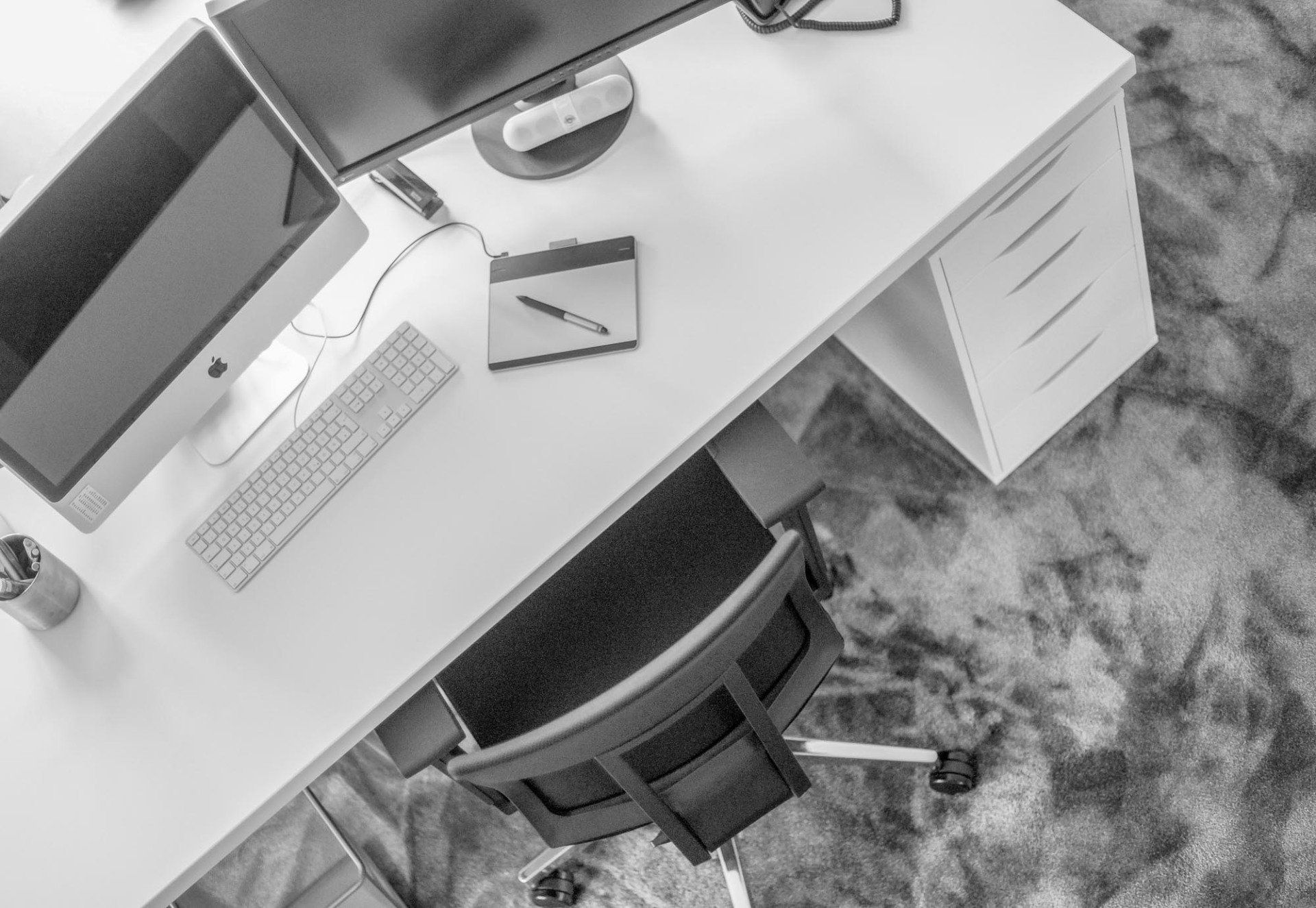 Ein Schwarzweißfoto eines Schreibtisches mit Computer, Tastatur und Stuhl.