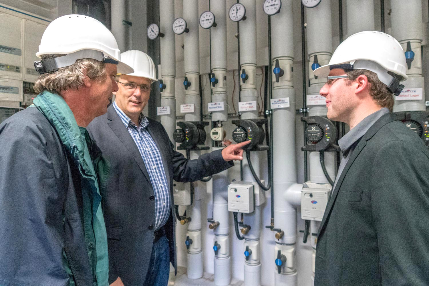 Drei Männer mit Schutzhelmen stehen nebeneinander in einem Raum.