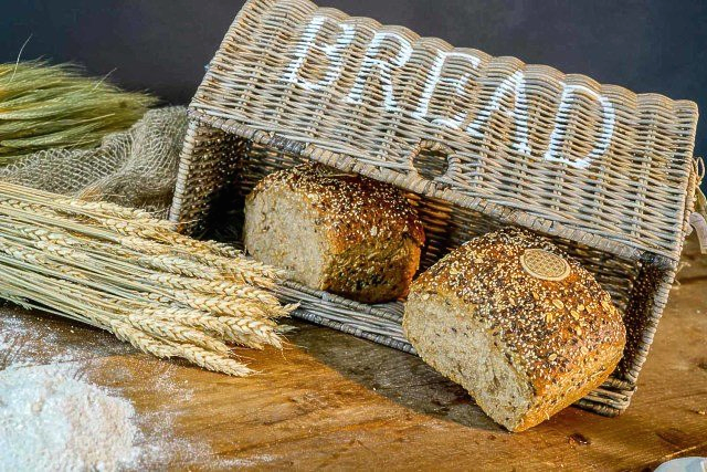 Zwei Brote liegen in einem Weidenkorb auf einem Holztisch.