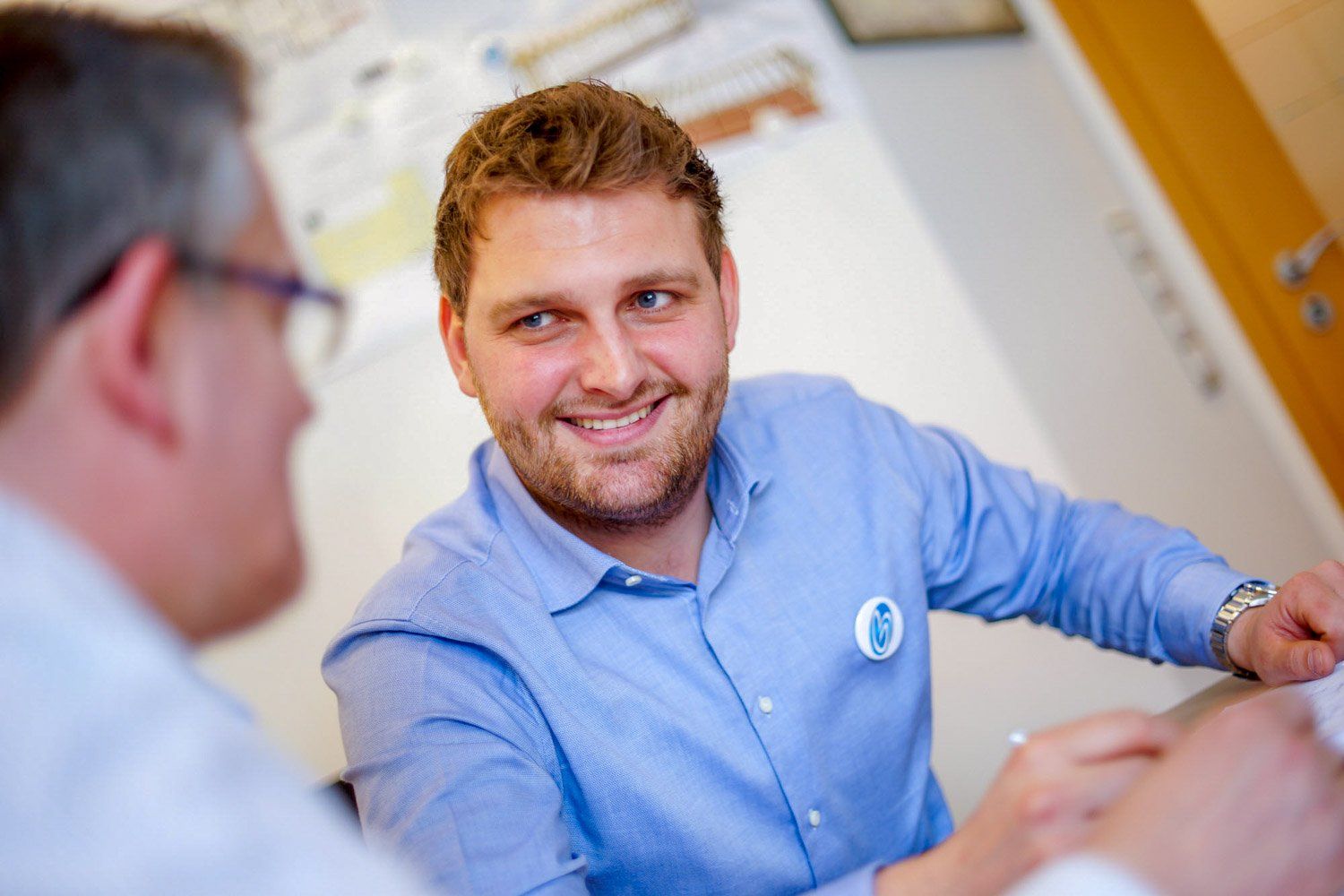 Ein Mann in einem blauen Hemd sitzt mit einem anderen Mann an einem Tisch.