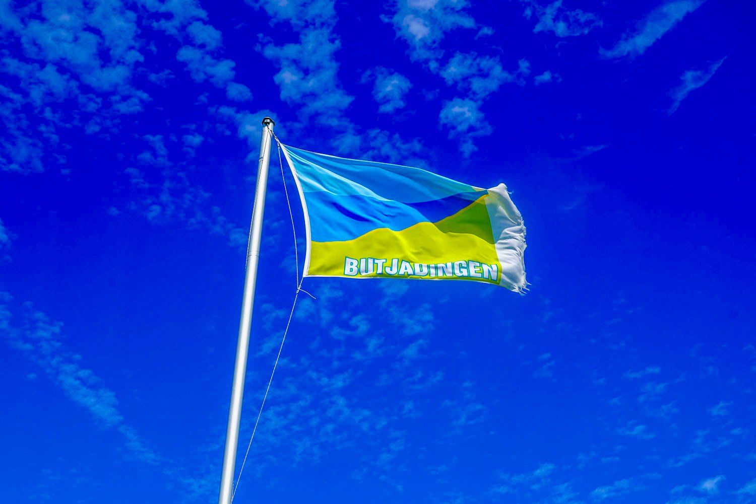 Eine blau-gelbe Flagge weht im Wind vor einem blauen Himmel.