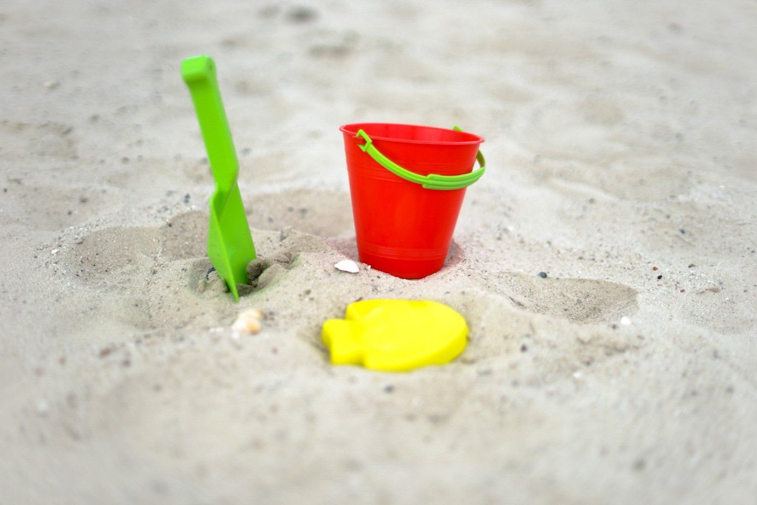 Ein roter Eimer und eine grüne Schaufel liegen im Sand am Strand.