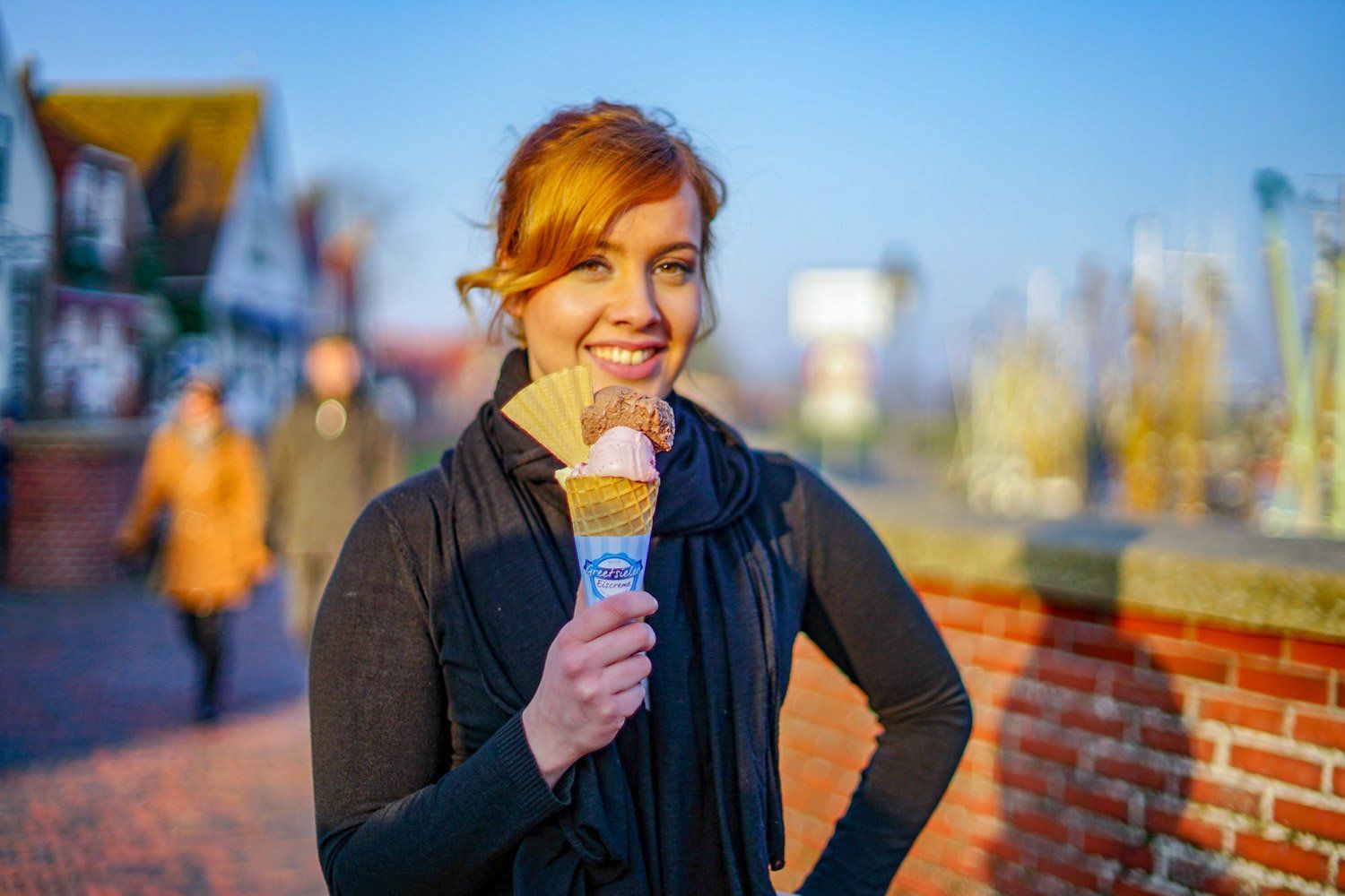 Eine Frau hält eine Eistüte vor einer Backsteinmauer.