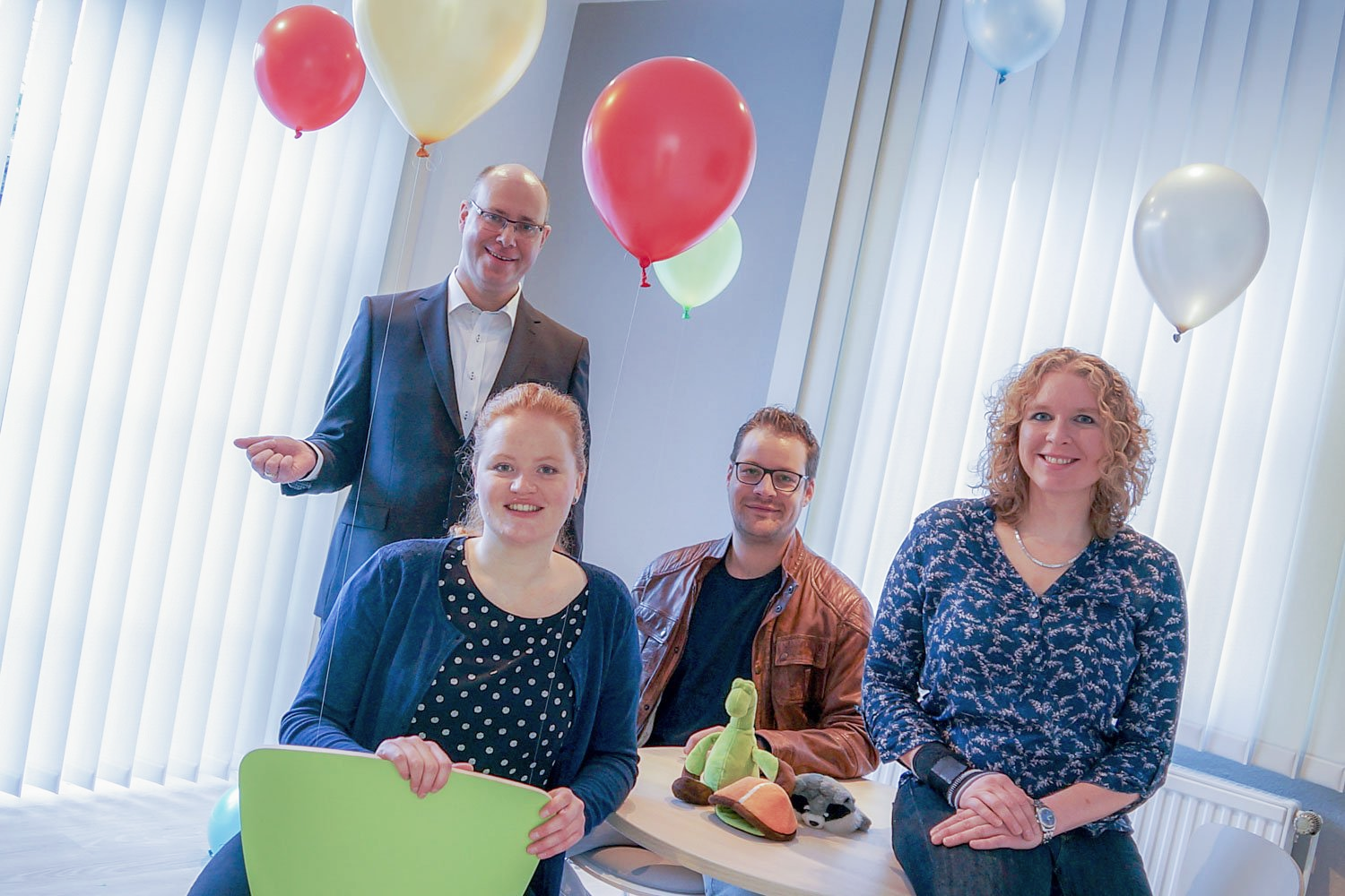 Eine Gruppe von Menschen sitzt an einem Tisch, im Hintergrund sind Luftballons zu sehen.