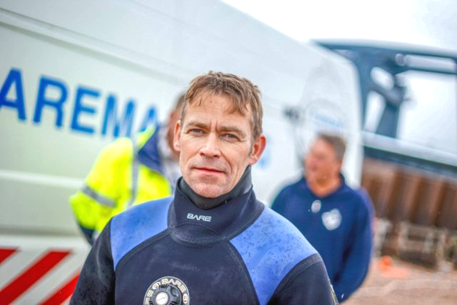 Ein Mann im Neoprenanzug steht vor einem Lieferwagen mit der Aufschrift „Arema“