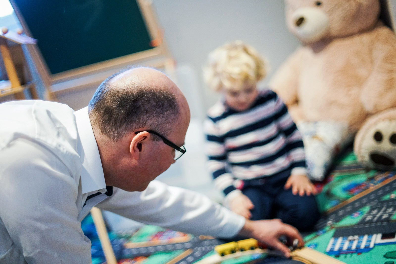 Ein Mann spielt mit einem Kind und einem Teddybären auf dem Boden.