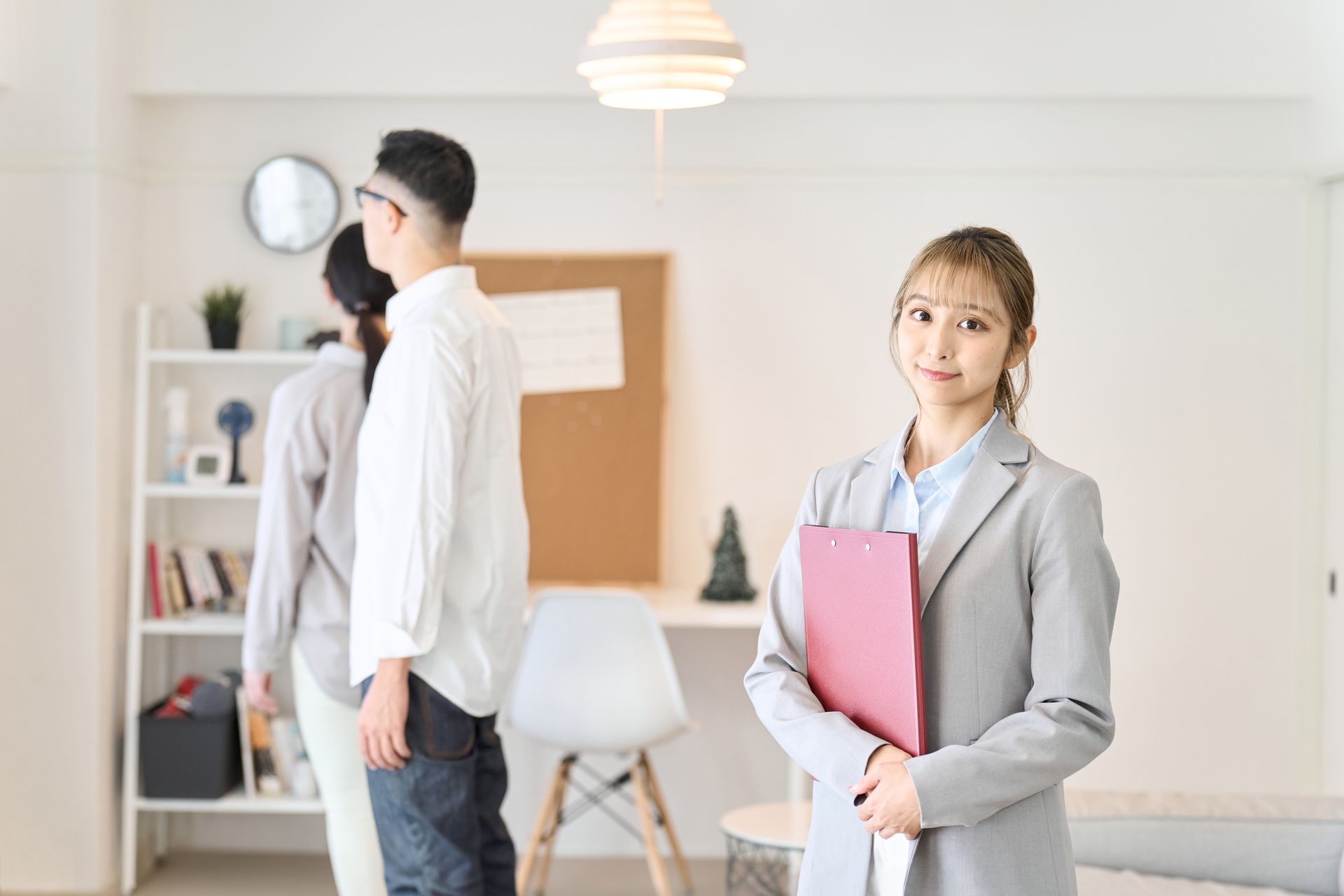 Real estate agent smiling, holding a folder, with a couple viewing a home.