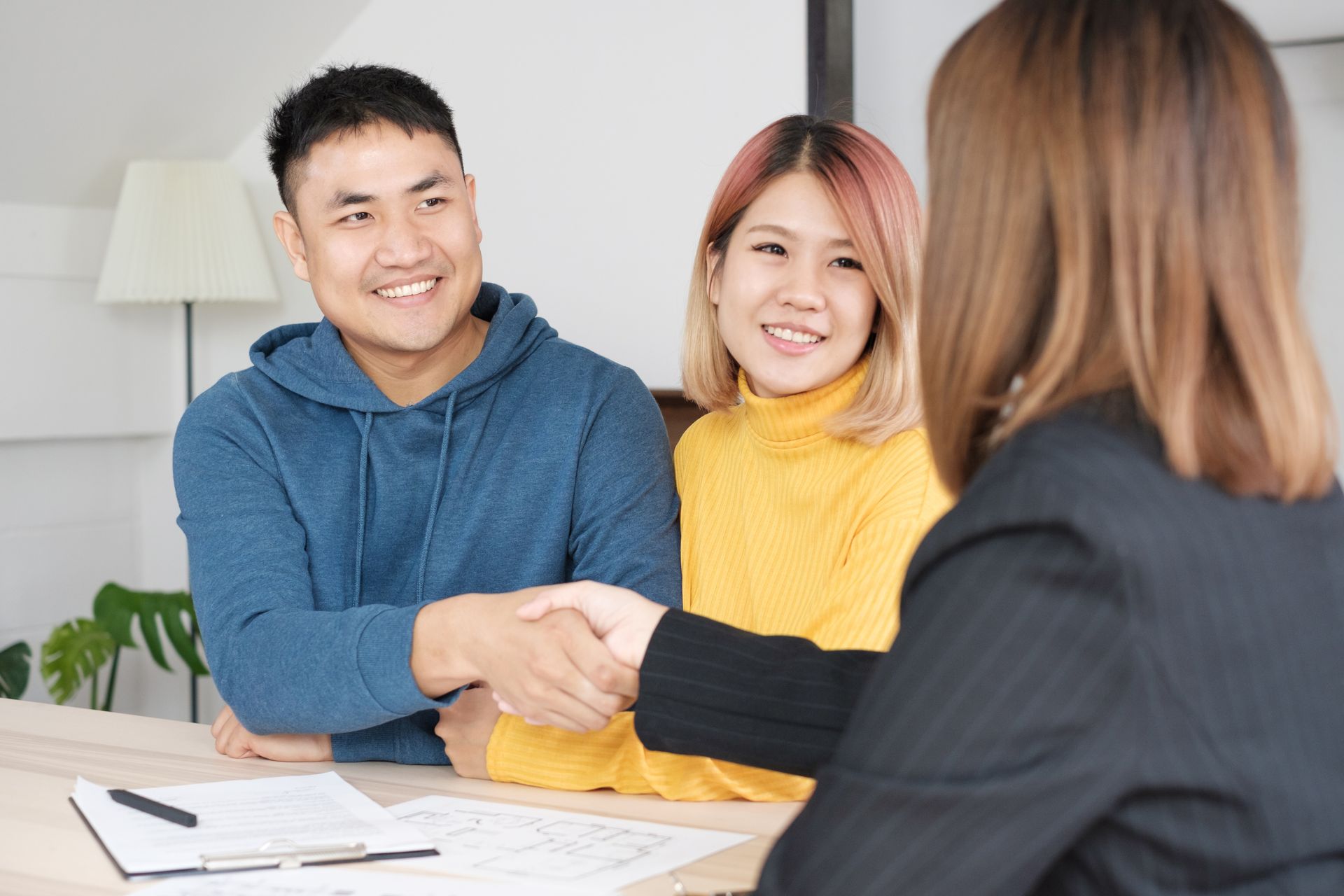 Couple shaking hands with a professional woman, smiling, indoors at a table.