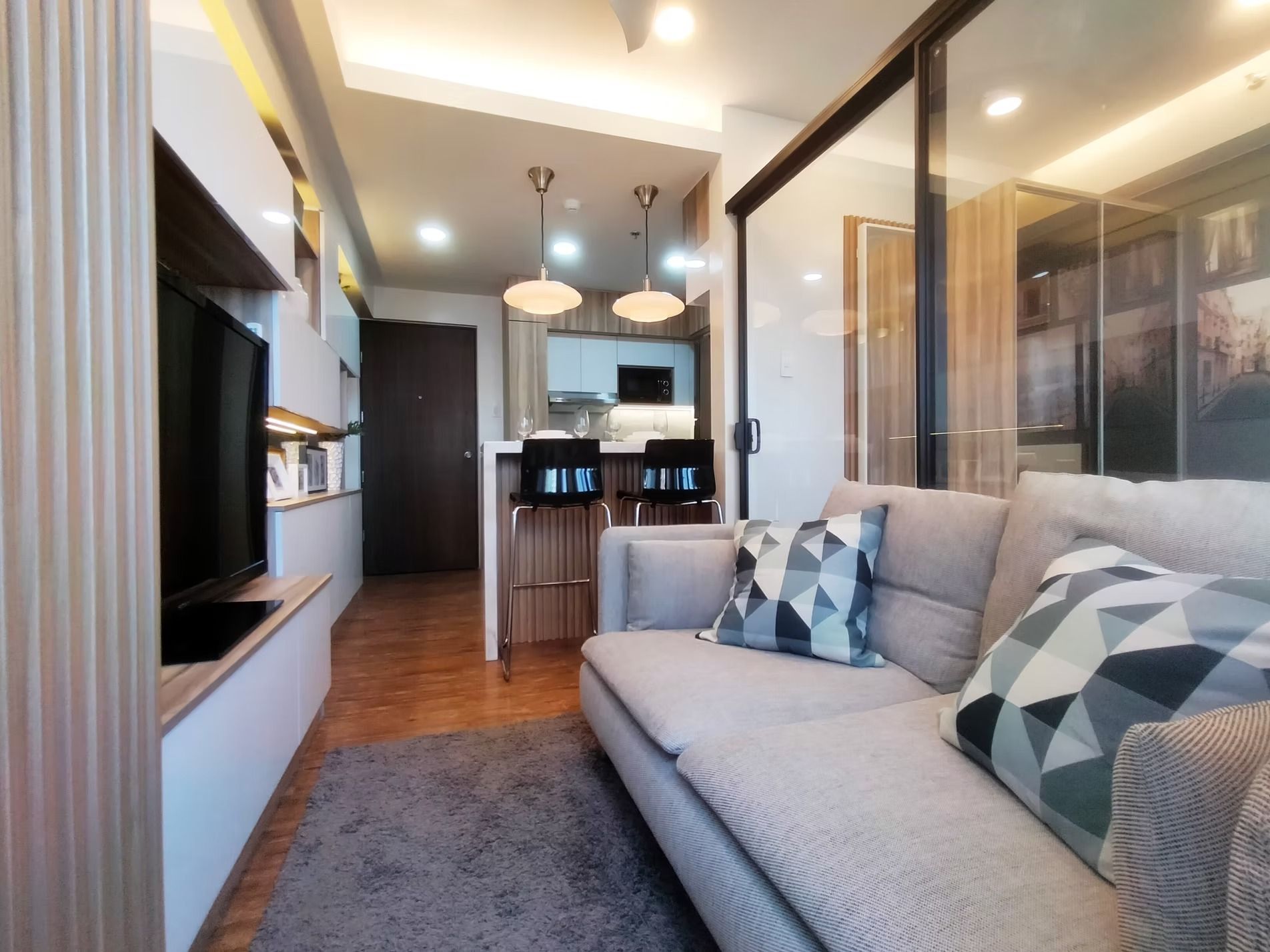 Cozy living room with a gray sofa, a TV, and a kitchen visible through a glass partition.