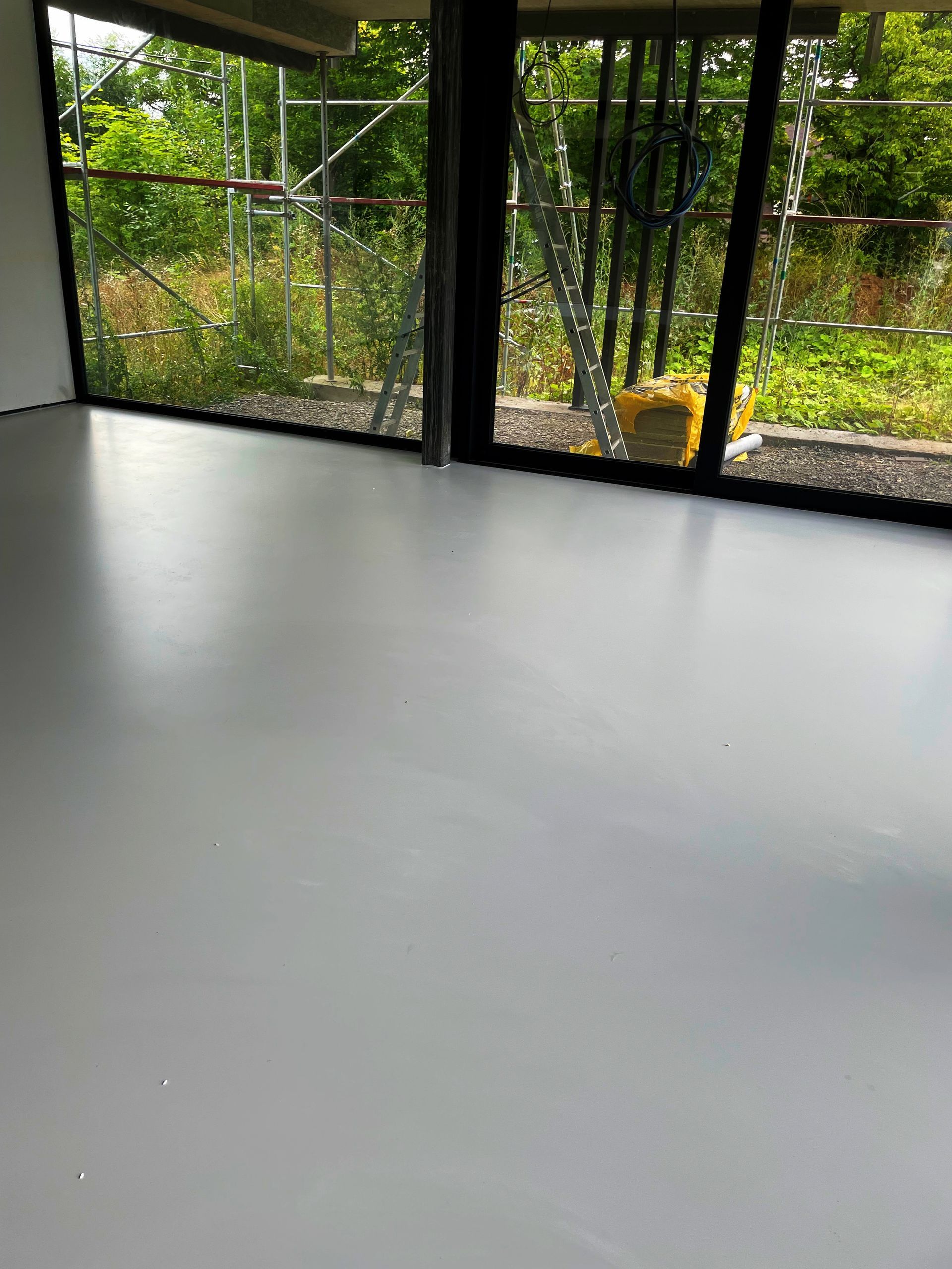 Šedá stěrková podlaha uvnitř budovy s oknem s výhledem do venkovní zahrady.