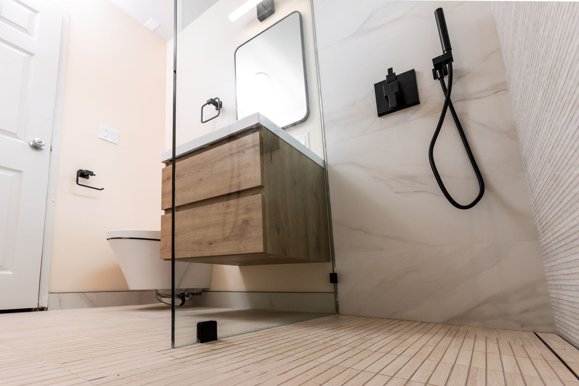 Modern bathroom with floating wooden vanity, glass shower, and patterned tile floor.