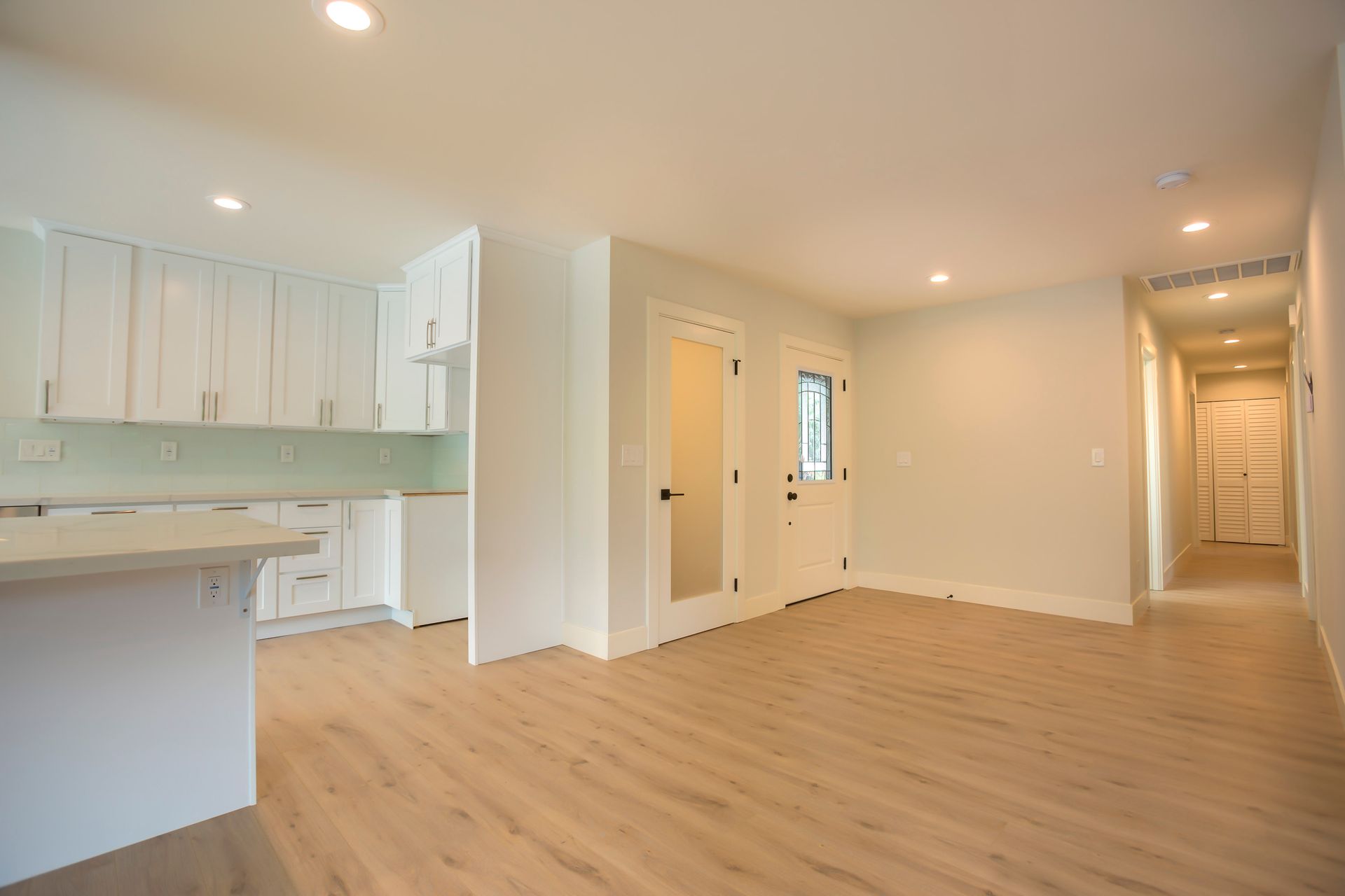 Interior of a newly renovated, bright white kitchen and living space with wood flooring.