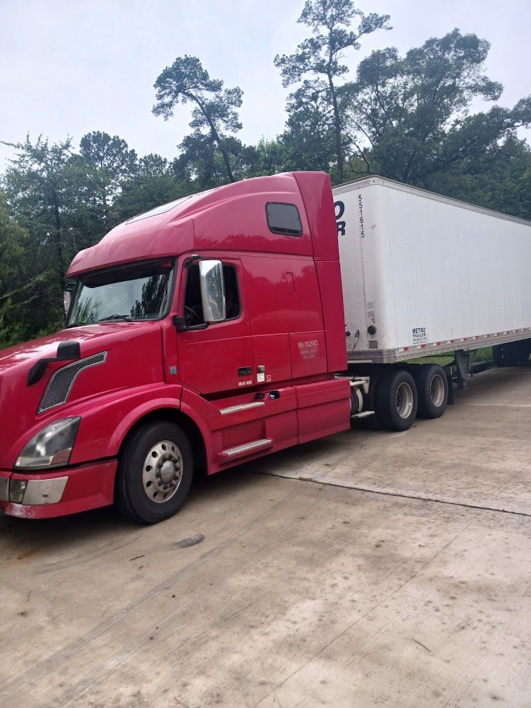 A red semi truck with a white trailer is parked in a parking lot.