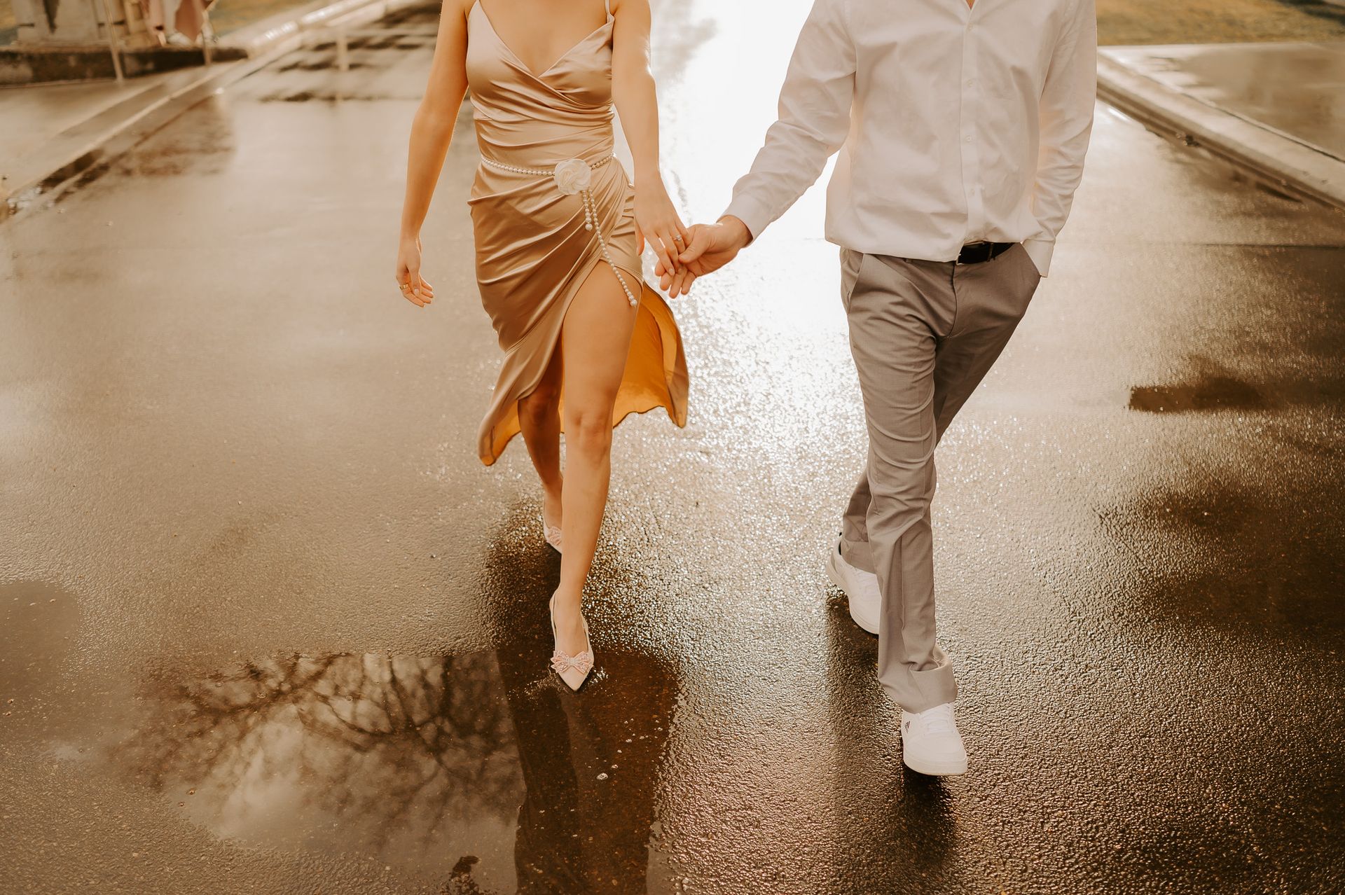 A man and a woman are holding hands while walking down a wet street.