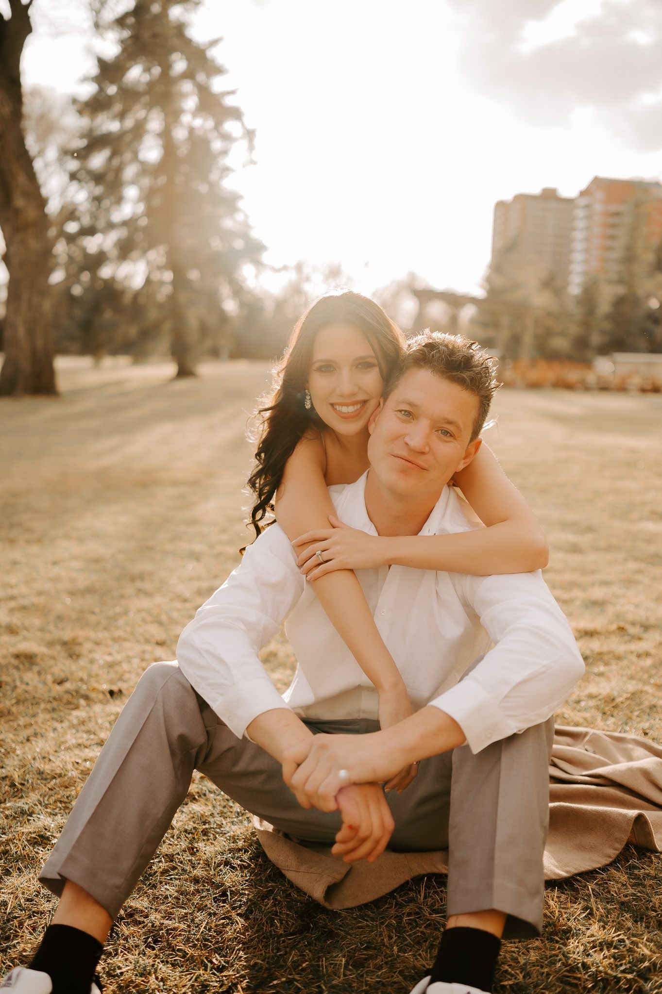 A man is sitting on the grass with a woman on his back.