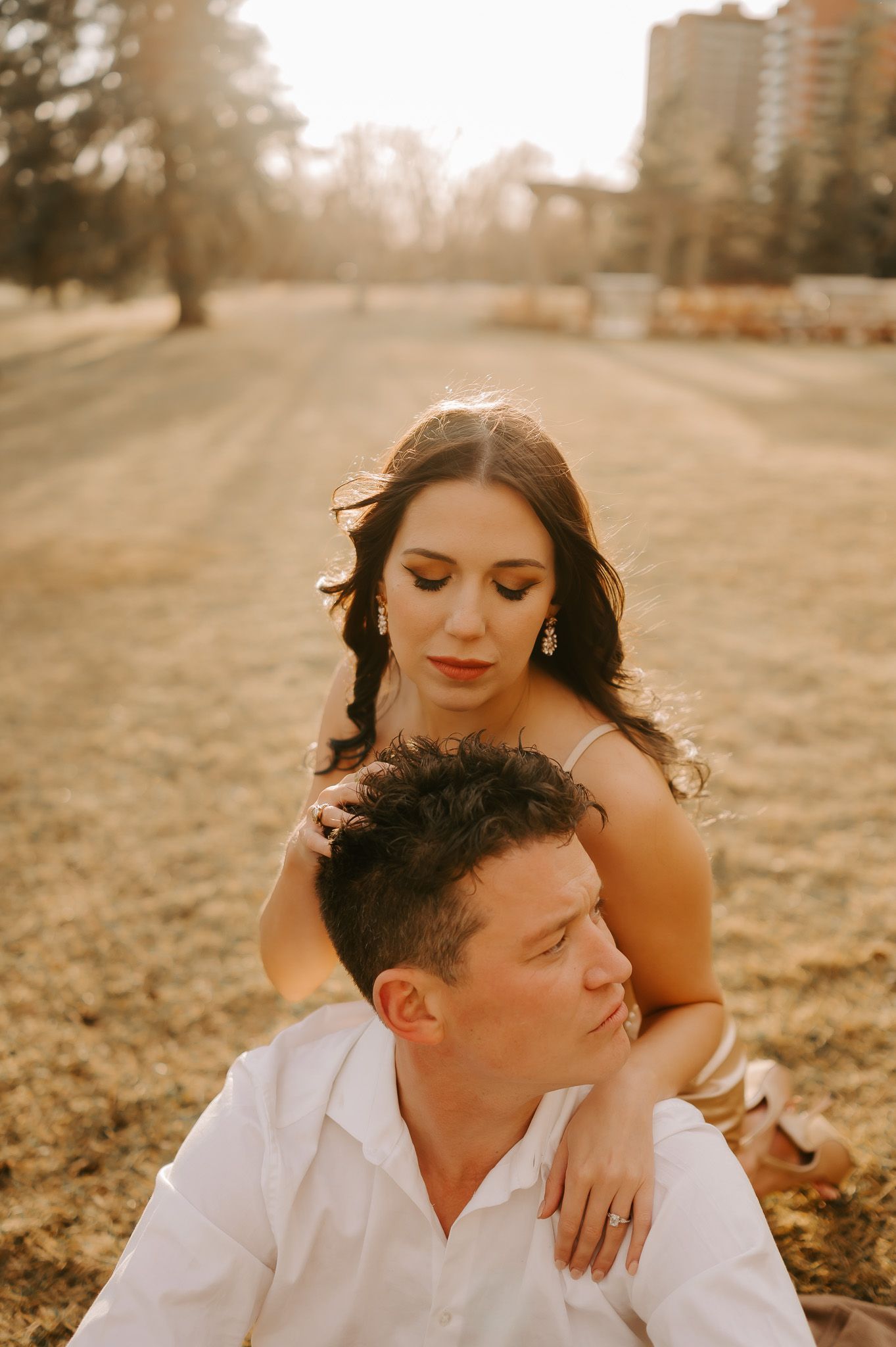 A man and a woman are sitting on the ground in a field . the woman is kissing the man on the cheek.