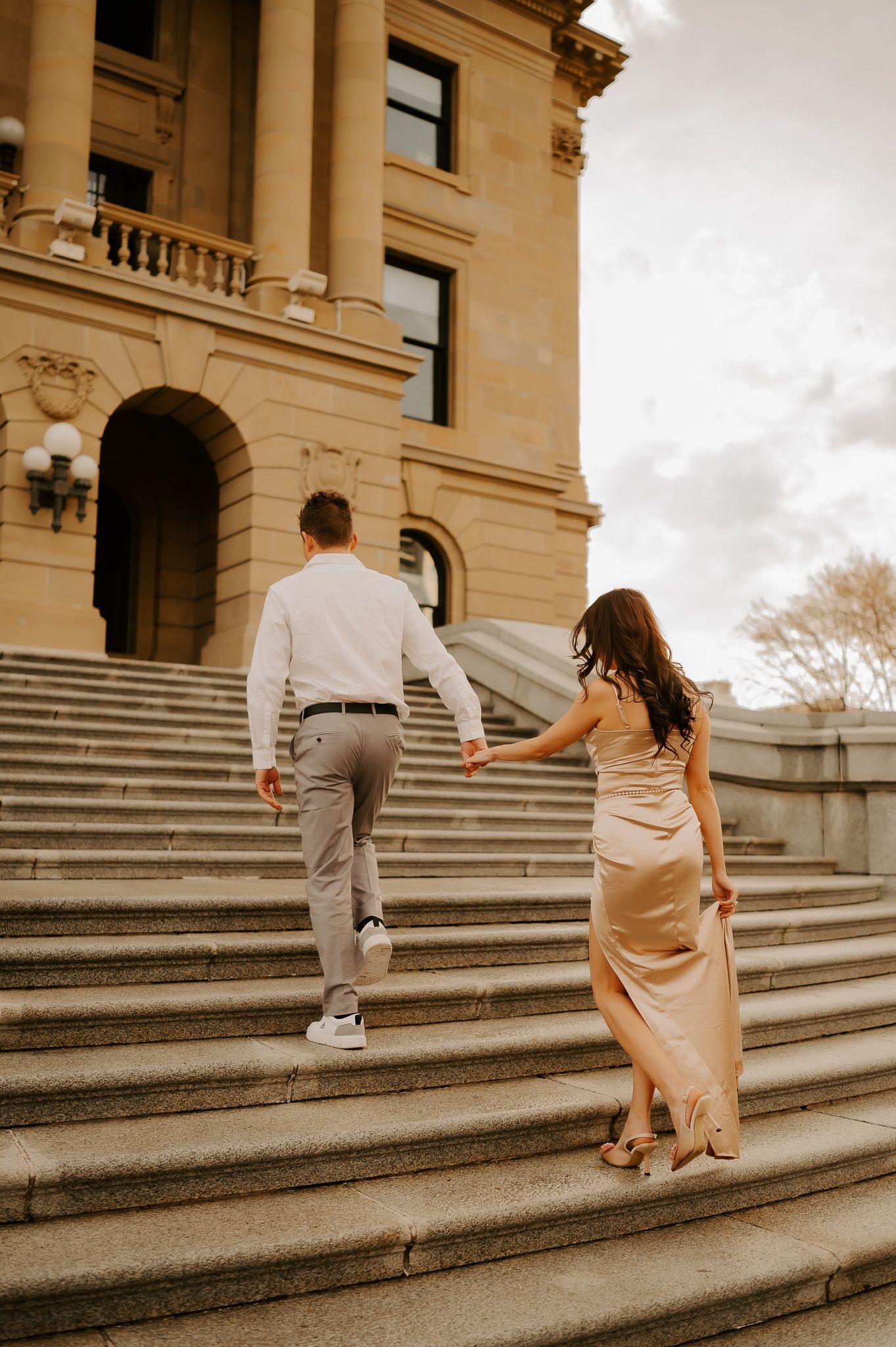 A man and a woman are walking up the stairs of a building holding hands.