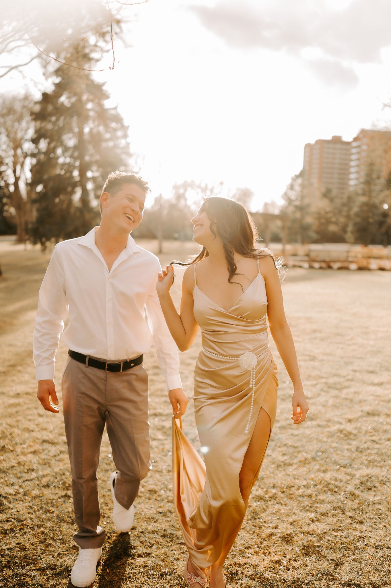 A man and a woman are walking in a park . the woman is wearing a gold dress.