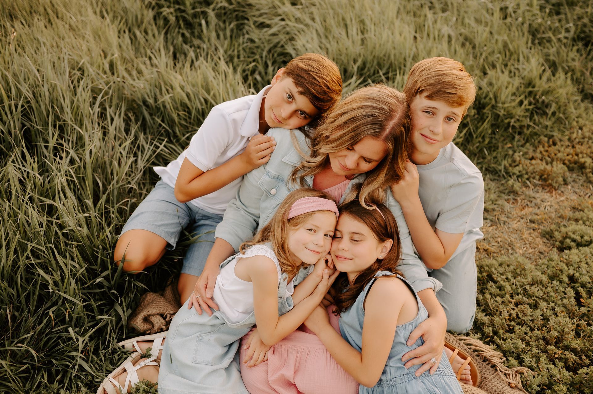 A family is sitting in the grass hugging each other posing for a family photo.