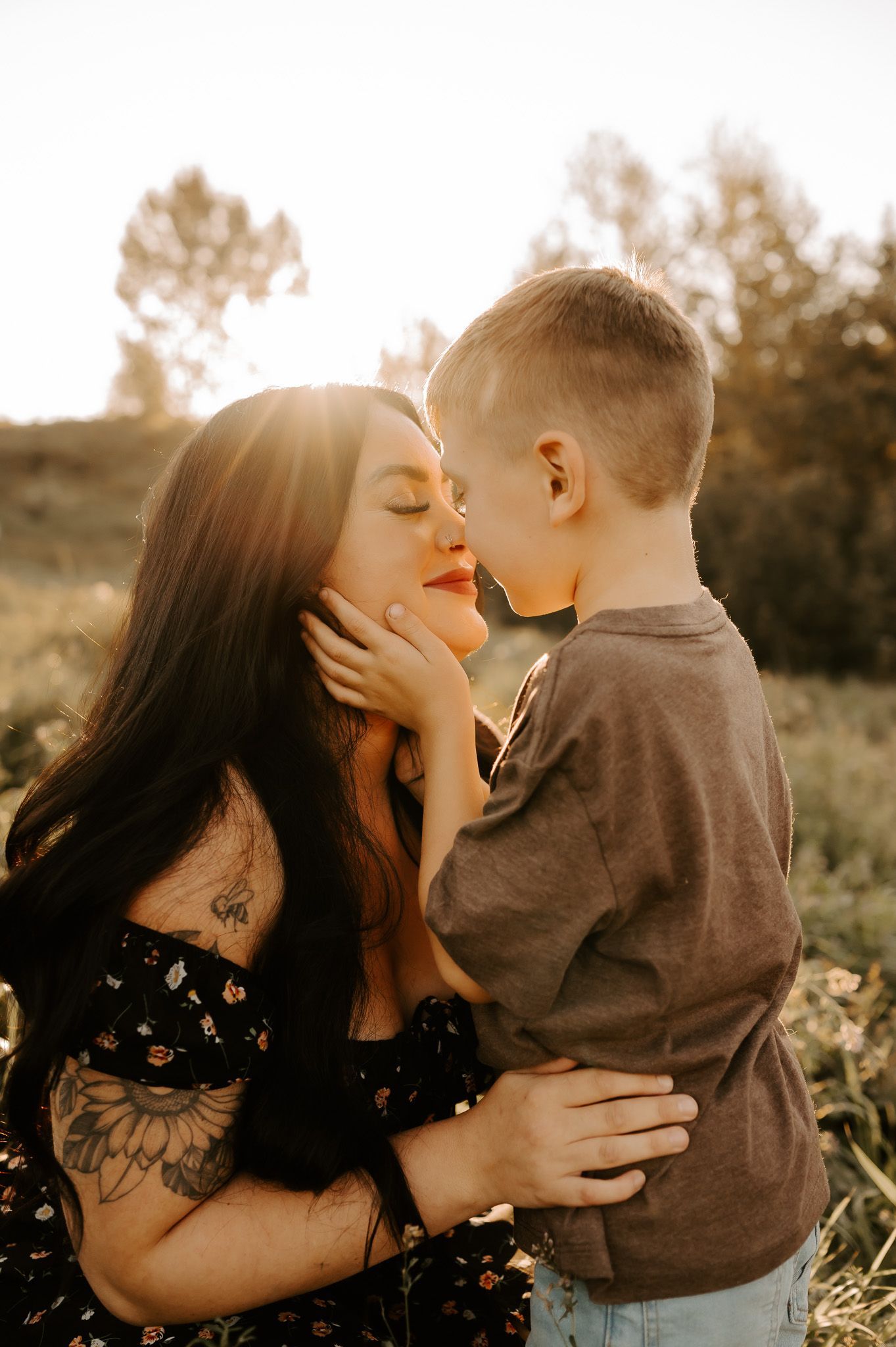 A photo of a family laughing together with their two kids on a grassy hill with golden sunset rays shining behind them.