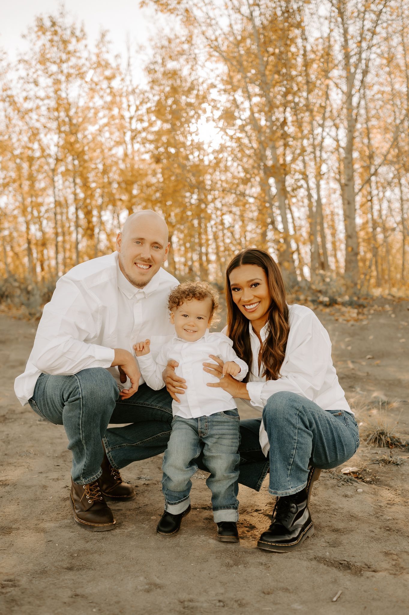 Family photography of a dad holding his son upside down while the daughter kisses the cheek while they laugh in a grassy field.