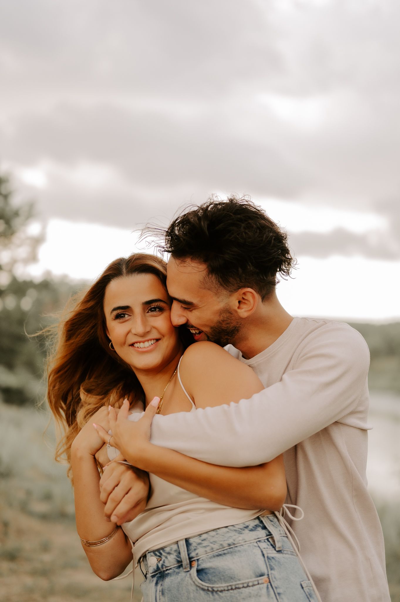 Photography of a couple posing. The Girl is on his back smiling as they stand in the sunset overlooking the Edmonton city skyline.