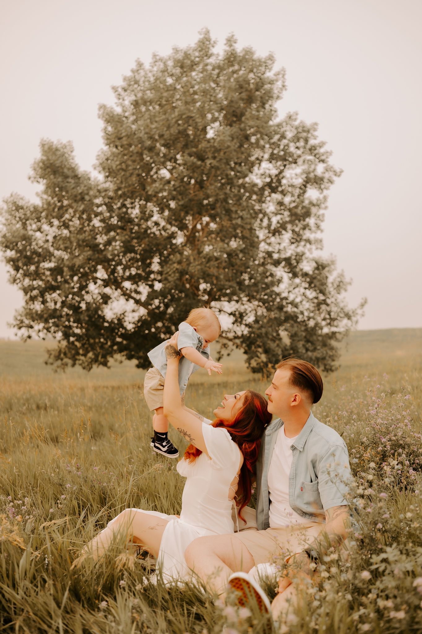  A father throws his laughing son up in the air while they're in a sunflower field. The mother holds their baby closely and admires them. 