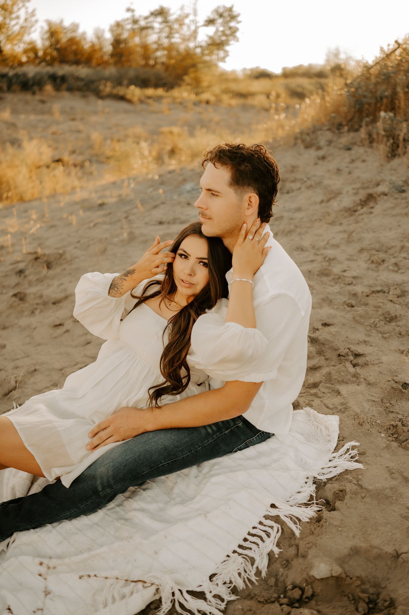 Engagement photography of a couple in Edmonton holding each other's faces, smiling as the sun shines through between them.